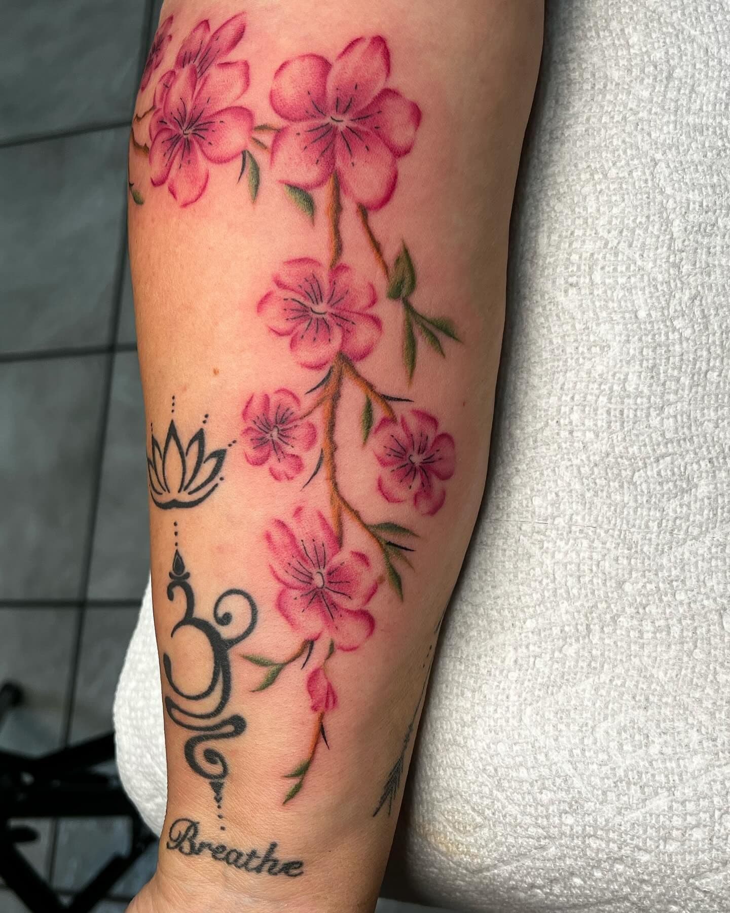 Colorful cherry blossom tattoo on forearm with fine line script