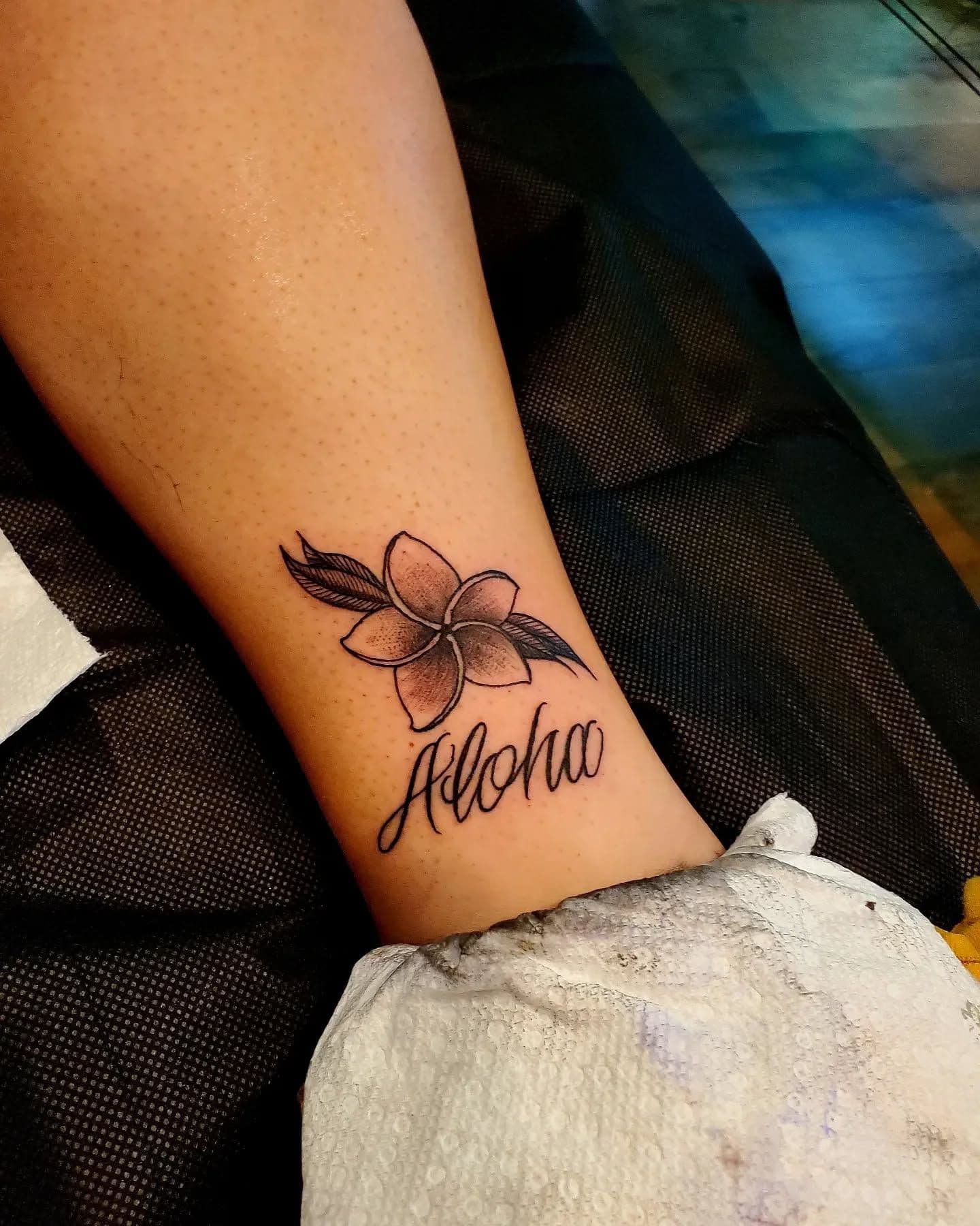 Black and grey plumeria with 'Aloha' script on calf.