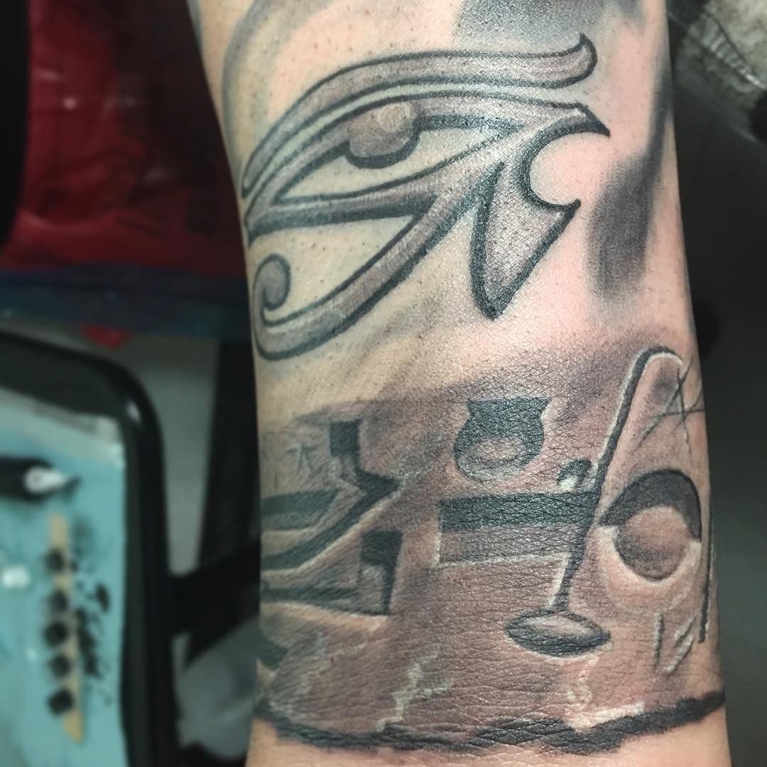 Black and grey Eye of Horus tattoo with hieroglyphs on forearm.