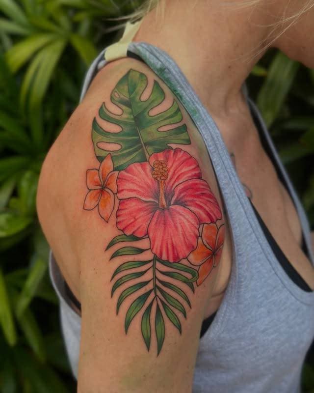 Colorful botanical tattoo of hibiscus and leaves on upper arm
